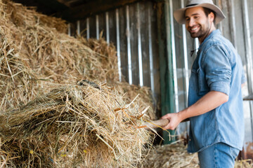 smiling farmer in brim hat stacking hay on blurred background.