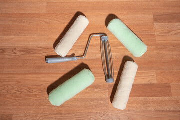 hand held metal roller with plastic comfort grip handle surrounded by four brand new fresh clean rolls, peach and mint green in color, prior to starting DIY home improvement project at house