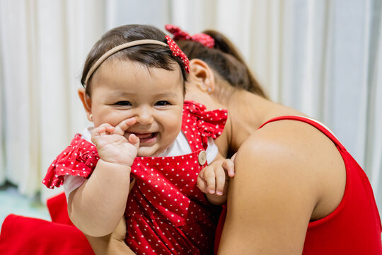 Portrait Of A Smiling Latin Baby Girl Looking At Camera, Her Mom Tickling Her