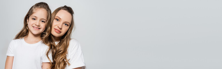 woman and smiling child with long hair looking at camera isolated on grey, banner.