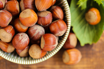Hazelnuts close-up in a green cup on a wooden table. Whole nuts with green leaves. Fresh harvest of hazelnuts. Farmed organic hazelnuts. Healthy fats.Hazelnuts harvest.view from above. 