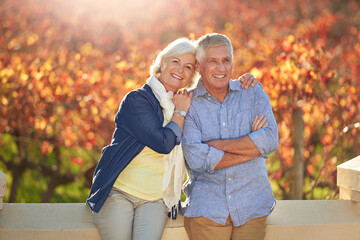 Enjoying their autumn years. Portrait of a smiling senior couple standing together in front of a vineyard in the autumn.