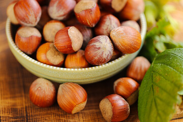 Hazelnuts close-up in a green cup on a wooden table. Whole nuts with green leaves. Fresh harvest of hazelnuts. Farmed organic ripe hazelnuts. Healthy fats