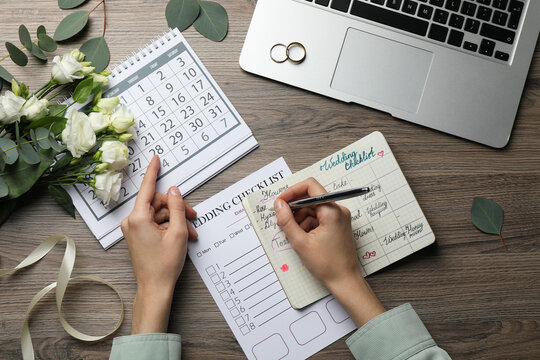 Woman filling Wedding Checklist in planner at wooden table, top view