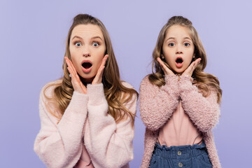 shocked mother and daughter looking at camera isolated on purple.