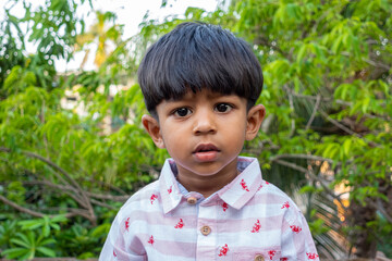 A boy is standing in the garden and eating a ripe banana. Boy eating food. Asian boy eating banana.