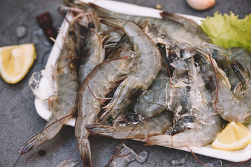 Raw shrimps on plate plastic tray, Fresh shrimp prawns for cooking with spices lemon vegetable salad lettuce on dark background in the seafood restaurant