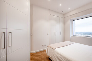 Fototapeta na wymiar teen bedroom with white down comforter, bay window with city view and white wood built in cabinets