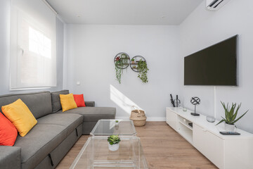 living room with three-seater sofa, white wooden furniture, tv on a table, methacrylate side tables, decorative plants and colored cushions on the sofa