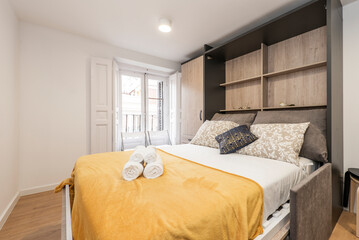wardrobe with pull down bed in study with white wooden balcony doors and yellow towel and rolled...