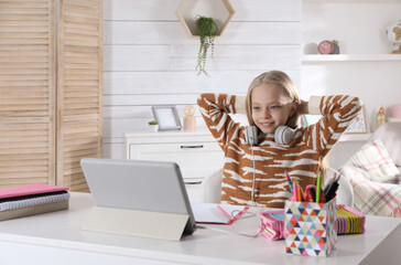 Cute little girl with modern tablet studying online at home, space for text. E-learning