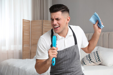 Man with brush and rag singing while cleaning in bedroom