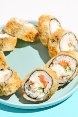 Tempura maki roll with salmon and eel on ceramic plate. Hot sushi with eel, salmon, cheese and cucumber inside. Modern japanese menu concept. Maki sushi on coloured background with chopsticks.