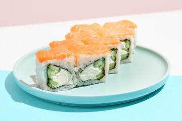 Classic sushi roll with salmon outside, cheese and cucumber inside. Philadelphia maki in minimal style. Modern japanese menu concept. Salmon maki roll on ceramic plate on coloured background.