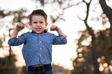Niño feliz contento divertido haciendo fuerza con sus brazos en el parque al aire libre en el...