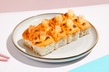 Hot maki roll with cheese on coloured background. Baked sushi roll with salmon inside, rice outside, cheese topped. Maki sushi in minimal style. Japanese menu concept.