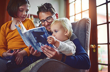 They enjoy story time as a family. Shot of father reading a book with his little son and daughter...