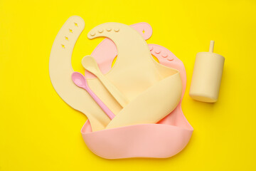 Baby feeding accessories and bibs on yellow background, flat lay