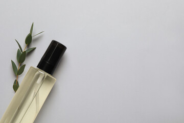 Bottle of baby oil and leaves on light grey background, flat lay. Space for text