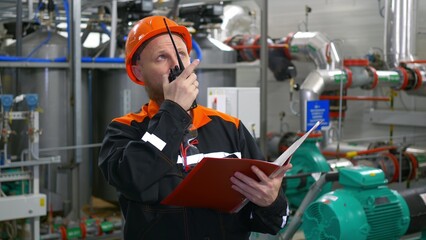 An industrial operator at a manufacturing plant inspects the equipment and transmits readings via...