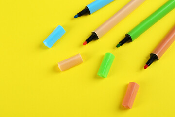Many colorful markers on yellow background, flat lay. School stationery