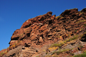 Layered rock formations on top of a hill overlooking a clear blue sky in summer.