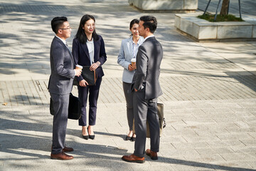 group of four asian business people men and women standing chatting talking outdoors on street - obrazy, fototapety, plakaty