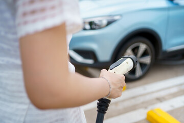 Happy Asian woman holding a DC - CCS type 2 EV charging connector at EV charging station.