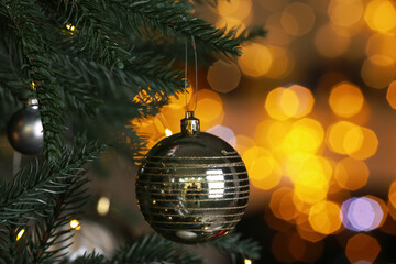 Beautiful shiny holiday bauble hanging on Christmas tree against blurred fairy lights, closeup. Space for text