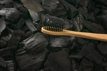 Wooden toothbrush with charcoal toothpaste on charcoal background.