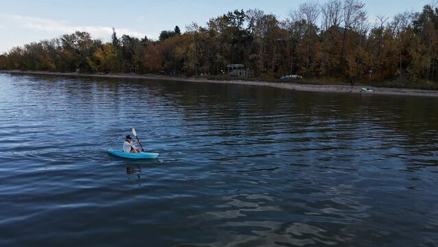 Woman in a kayak paddling along the vibrant shoreline of buffalo lake in autumn. Aerial pull back shot revealing the colourful foliage
