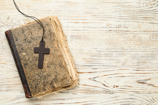 Wooden Christian cross and old Bible on white table, top view. Space for text