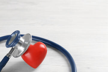 Stethoscope and red heart on white wooden table, closeup with space for text. Cardiology concept