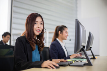 Young Asian business call center man and woman with headset sitting in office desk using computer....