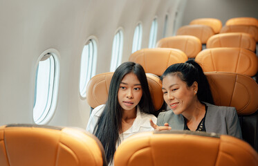 Smiling elegant asian woman talking while passenger seat near window in airplane.