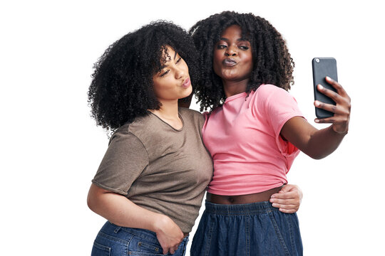 Best friends make the best profile pics. Studio shot of two young women using a smartphone to take selfies against a white background.