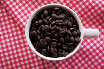 Flat lay of coffee beans in white ceramic cup on red tablecloth