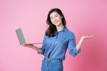 Young Asian businesswoman using laptop on pink background