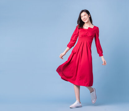 Full length image of young Asian woman wearing red dress on blue background