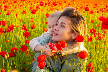 Mother with daughter hugging on the poppies meadow. Beautiful mom and daughter on a poppy field outdoor. Mother and daughter on spring poppies flowers.