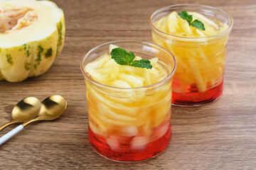 Es Blewah or contain slices of cantaloupe with syrup. Served in glass on wooden table.
