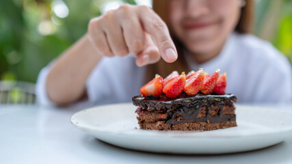 Blurred image of a young woman eating and pointing finger at a piece of strawberry chocolate cake