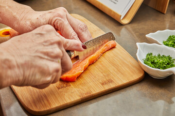 Chef cuts the salmon with knife into strips to prepare the dish according to the recipe