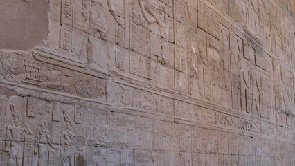 The wall of the ancient temple of Horus in Edfu. Close-up. Carvings of gods and hieroglyphs are visible. Egypt. - obrazy, fototapety, plakaty