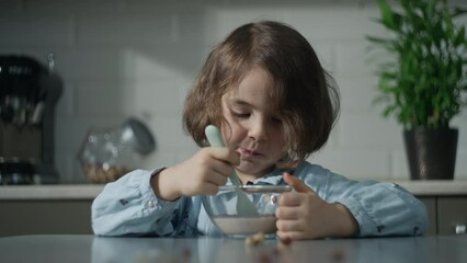 Caucasian child girl having breakfast in the kitchen. Beautiful little girl eats a spoonful of breakfast cereal with milk.