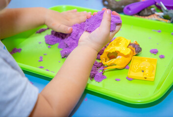 A girl of European appearance plays with lilac kinetic sand