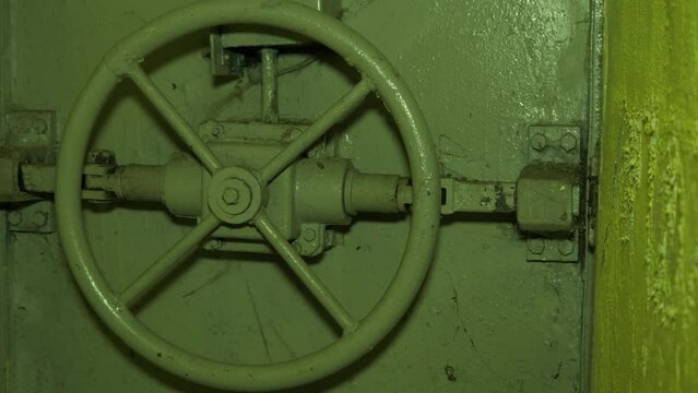 Steel door lock inside the concrete bomb shelter to hide civil people, an underground apocalypse bunker built in old coastal fortification, medium handheld closeup dolly shot moving left