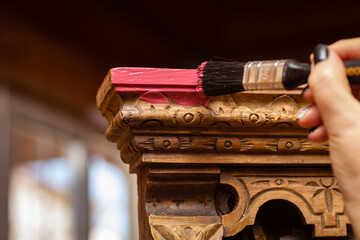 Paint brush going over carved ornaments surface on antique cupboard for kitchen. Re-usage of old furniture for sustainable future. Hobby of furniture restoration.