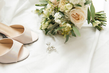 A luxurious bridal bouquet with white roses next to shoes and accessories on a light background