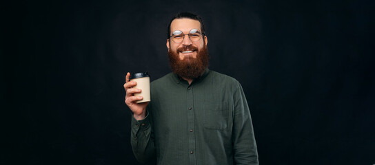 Panorama photo of a bearded hipster man enjoying his cup of coffee to go. Studio shot over black background.